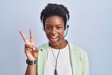 Sticker - African american woman wearing call center agent headset smiling with happy face winking at the camera doing victory sign with fingers. number two.