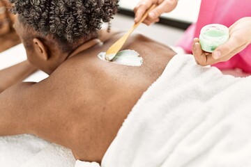 Canvas Print - African american woman lying on table having back massage using cream at beauty salon