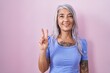 © Krakenimages.com - Middle age woman with tattoos standing over pink background showing and pointing up with fingers number two while smiling confident and happy.