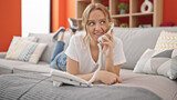 Fototapeta Psy - Young blonde woman talking on telephone lying on sofa at home