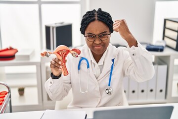 Wall Mural - African american doctor woman holding anatomical model of female genital organ annoyed and frustrated shouting with anger, yelling crazy with anger and hand raised