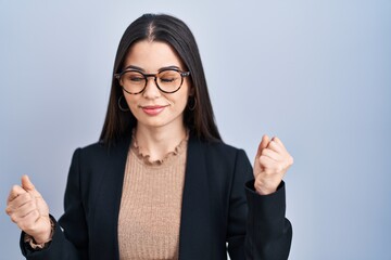 Poster - Young brunette woman standing over blue background very happy and excited doing winner gesture with arms raised, smiling and screaming for success. celebration concept.