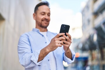 Wall Mural - Young caucasian man smiling confident using smartphone at street