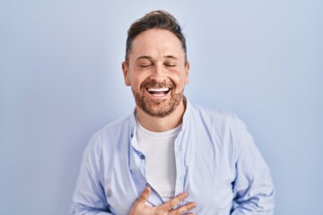 Sticker - Middle age caucasian man standing over blue background smiling and laughing hard out loud because funny crazy joke with hands on body.