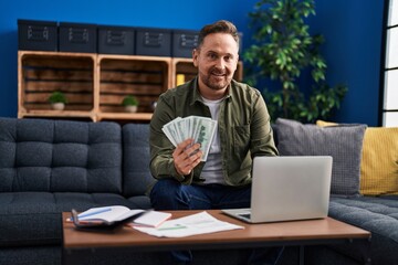 Sticker - Young caucasian man using laptop counting dollars at home