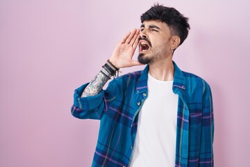 Sticker - Young hispanic man with beard standing over pink background shouting and screaming loud to side with hand on mouth. communication concept.