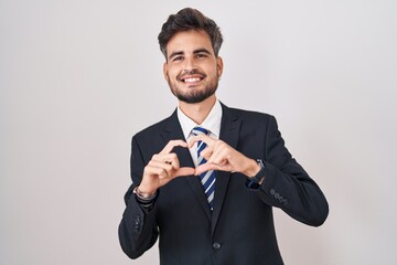 Poster - Young hispanic man with tattoos wearing business suit and tie smiling in love doing heart symbol shape with hands. romantic concept.