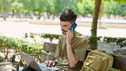 Sticker - Young hispanic man tourist using laptop talking on smartphone at park