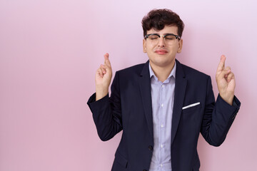 Poster - Young non binary man with beard wearing suit and tie gesturing finger crossed smiling with hope and eyes closed. luck and superstitious concept.