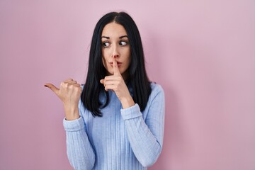 Sticker - Hispanic woman standing over pink background asking to be quiet with finger on lips pointing with hand to the side. silence and secret concept.