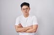 © Krakenimages.com - Young asian man standing over white background skeptic and nervous, disapproving expression on face with crossed arms. negative person.