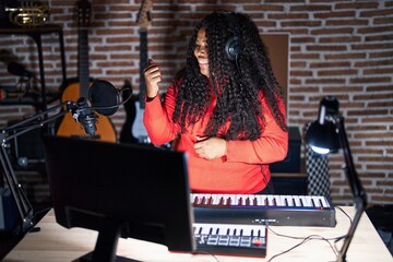 Sticker - Plus size hispanic woman playing piano at music studio smiling with happy face looking and pointing to the side with thumb up.