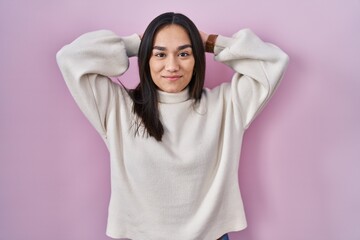 Poster - Young south asian woman standing over pink background relaxing and stretching, arms and hands behind head and neck smiling happy