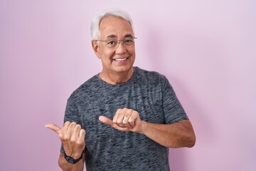 Wall Mural - Middle age man with grey hair standing over pink background pointing to the back behind with hand and thumbs up, smiling confident