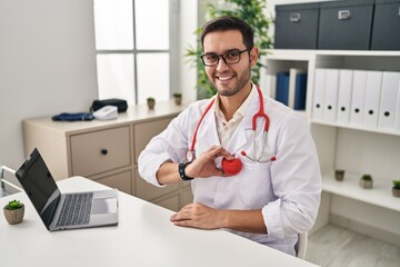 Sticker - Young hispanic man wearing doctor uniform holding heart over chest at clinic