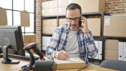 Canvas Print - Middle age man ecommerce business worker talking on smartphone writing on package at office