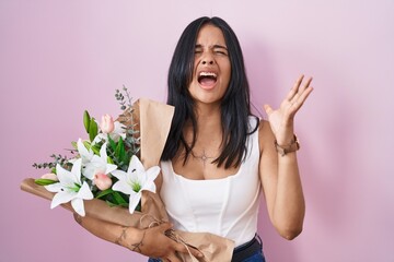 Canvas Print - Brunette woman holding bouquet of white flowers crazy and mad shouting and yelling with aggressive expression and arms raised. frustration concept.