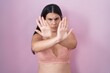 Young hispanic woman wearing pink bra rejection expression crossing arms and palms doing negative sign, angry face