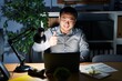 © Krakenimages.com - Young chinese man working using computer laptop at night doing happy thumbs up gesture with hand. approving expression looking at the camera showing success.