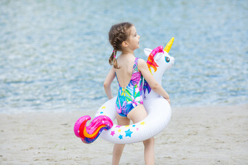 back view adorable happy smiling little girl on beach vacation with swimming ring unicorn