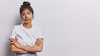 Studio shot of pleasant looking Iranian woman keeps arms folded concentrated aside with thoughtful expression wears casual t shirt isolated over white background copy space for your advertisement
