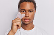 © WHstudio Leushin N - Headshot of dark skinned man uses gua sha stone for massaging wears casual t shirt concentrated attentively at camera isolated over white background. Alternative medicine and cosmetology concept