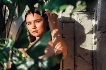 Wall Mural - Pretty young lady applying massage oil drops with pipette to face skin in shadow, looking at camera. Lovely woman with cosmetic oil at textured wall. Cosmetology self care concept. Copy ad text space