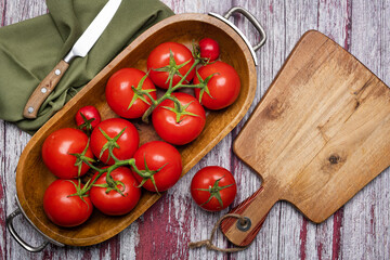 Wall Mural - Fresh tomatoes in a wooden bowl and a cutting board with a knife on a wooden table. View from above. Place for text.