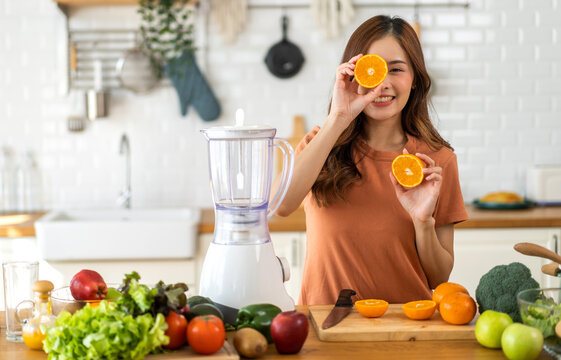 Portrait of beauty body slim healthy asian woman holding orange fruit slice hiding eye behind.young girl preparing cook healthy drink with orange juice in kitchen at home,Diet.Self love and Self care