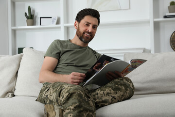 Wall Mural - Happy soldier reading magazine on sofa in living room. Military service