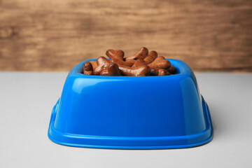 Blue bowl with bone shaped dog cookies on light table, closeup