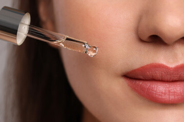 Wall Mural - Young woman applying essential oil onto face, closeup