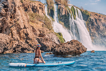 Wall Mural - Happy girl on a SUP board near huge Duden waterfall in Antalya, Turkey. Summer watersports and recreation and adventure concept