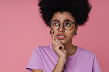 Wall Mural - Pensive afro woman touching her chin while standing isolated over pink wall