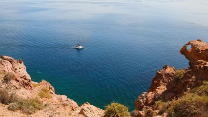 Wall Mural - Yacht sailing near the sea coast. Santorini island, Greece. Clear blue sea and red volcanic rocks. Summer seascape. Travel and vacation concept. 
