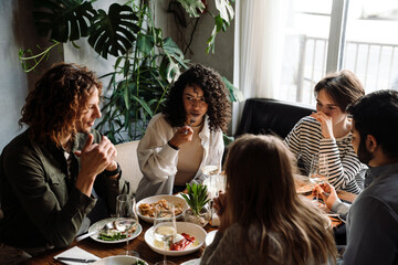 Wall Mural - Group of cheerful friends talking while dining in restaurant