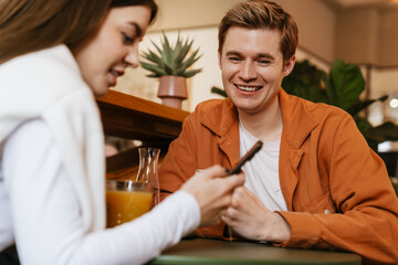 Wall Mural - Happy couple using mobile phone while sitting in cafe