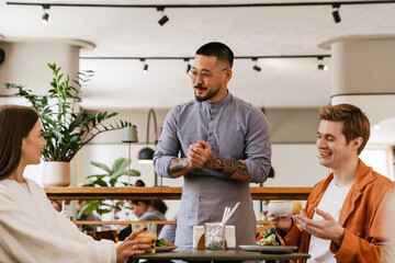 Wall Mural - Smiling waiter serving couple in cafe