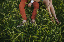 Couple Sitting Together On Green Grass. Boy's And Girl's Legs On Green Grass