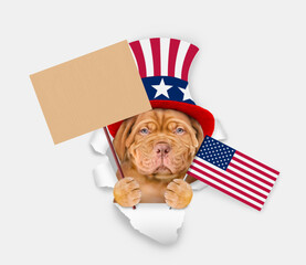 Poster - Serious Mastiff puppy wearing like Uncle Sam looking through a hole in paper and shows empty placard and flag USA. isolated on white background