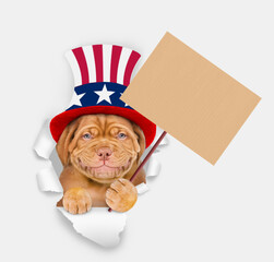 Poster - Smiling Mastiff puppy wearing like Uncle Sam looking through a hole in paper and shows empty placard. isolated on white background