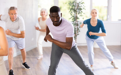 Wall Mural - African American man and friends people of different ages dancing in studio or gym doing sports or practicing dance number. Physical activity, good bodily shape