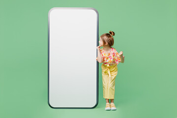 Full body happy little child kid girl 6-7 years old wear casual clothes big blank screen area mobile cell phone do winner gesture isolated on plain green background. Mother's Day love family concept.