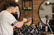 © Aleksandr - Back view of handsome hairdresser cutting hair of man. Hairstylist serving client at barber shop.