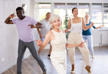 Wall Mural - Smiling senior woman dancing vintage twist, popular in sixties, with characteristic arm movements in modern dance studio. Nostalgia for youth. Active hobbies concept