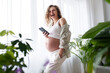 © Westend61 - Happy pregnant woman with hand in pocket holding smart phone at home