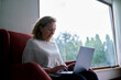 © Westend61 - Senior woman using laptop sitting in armchair at home
