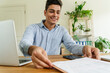 © Westend61 - Smiling young businessman looking at document on desk in office