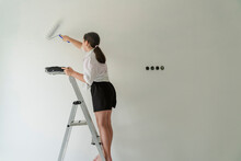 Girl Standing On Ladder And Painting Wall At Home