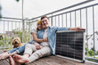 © Westend61 - Happy couple sitting with solar panel and dog